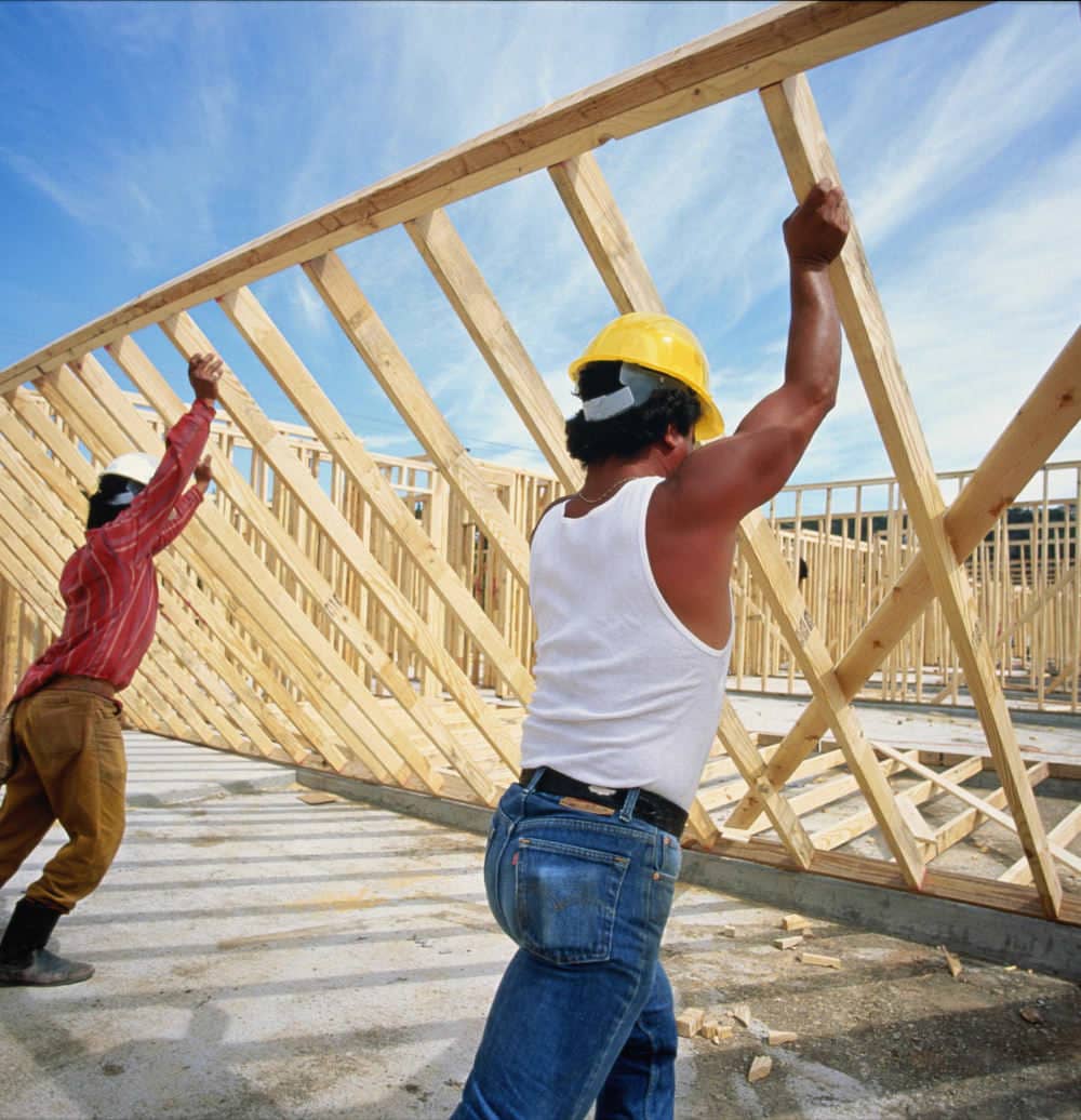 Construction team raising a timber roof truss on a new build site